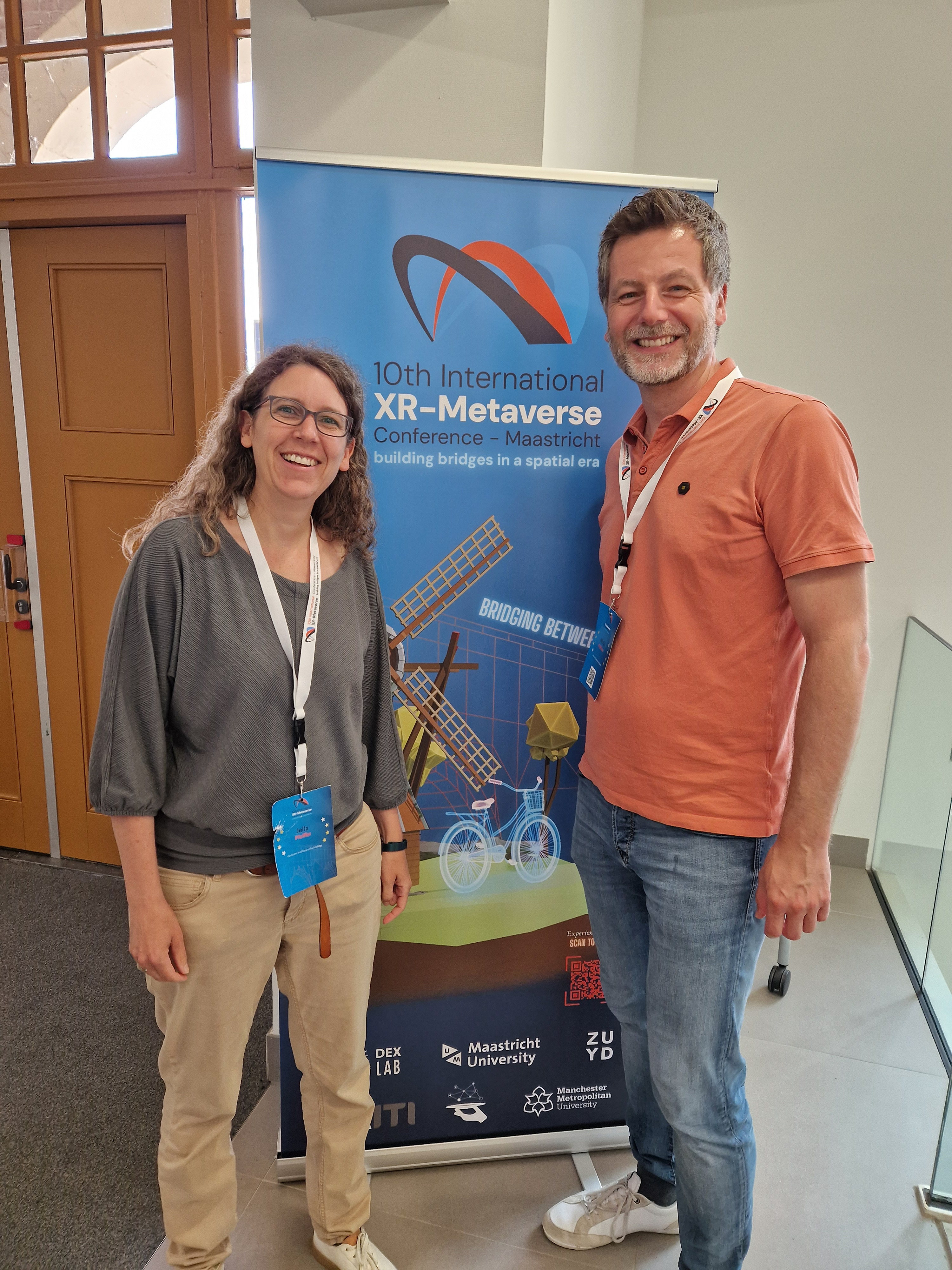 Prof. Jella Pfeiffer and Prof. Martin Meißner pose in front of a banner for the 10th International XR-Metaverse Conference.