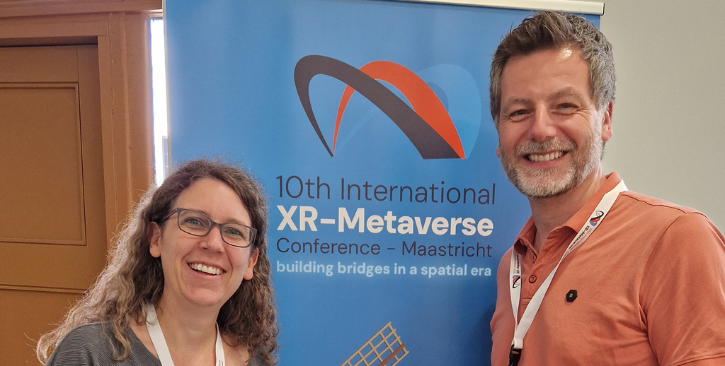 Prof. Jella Pfeiffer and Prof. Martin Meißner pose in front of a banner for the 10th International XR-Metaverse Conference.
